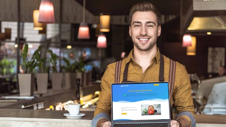 A man standing in a cafe holds a laptop displaying a search engine optimization webpage for an SEO company in Toronto.
