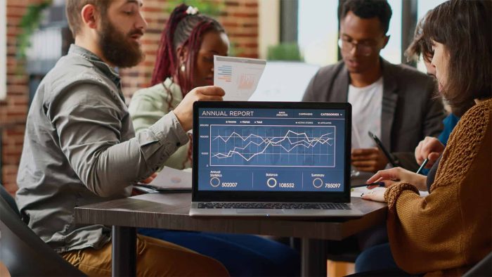 A group of people sit around a table in discussion, with a laptop displaying an annual report and data charts in the foreground at a leading SEO company in Toronto.